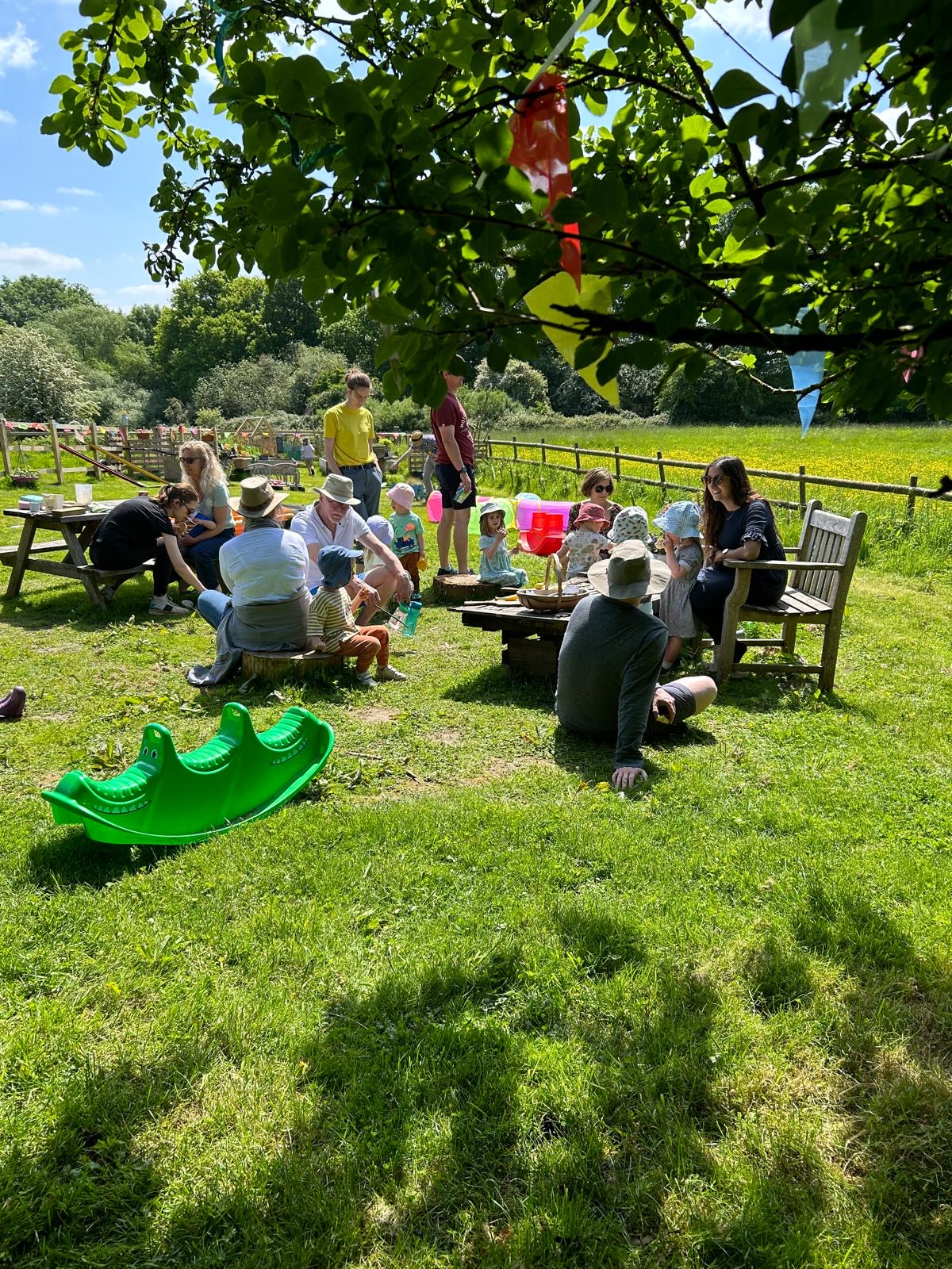 Families gathered under a tree with bunting on a sunny morning