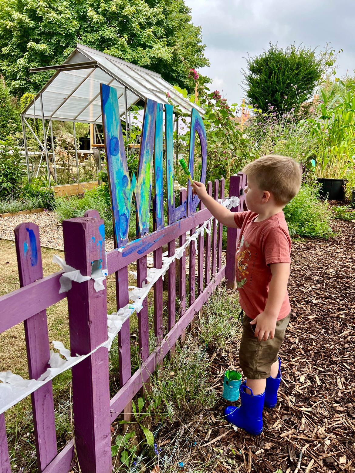 A boy painting the WILD sign blue on a purple fence