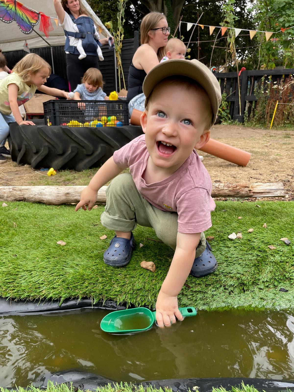 A toddler laughing while scooping water from a muddy pond