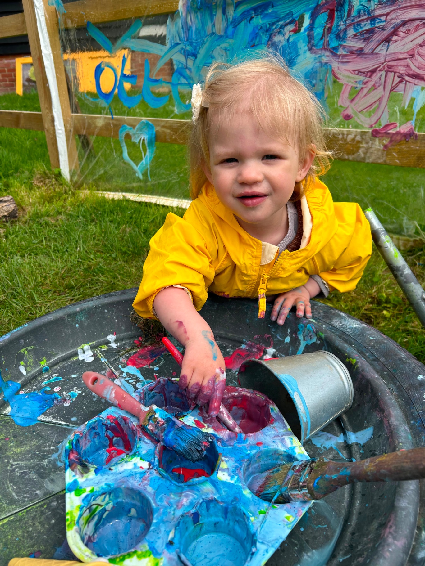 A toddler in a yellow raincoat painting outdoors