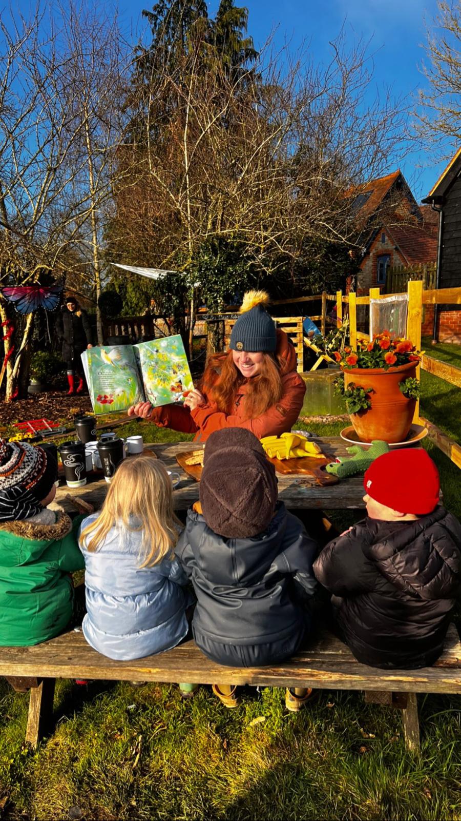 Children sitting at a picnic bench listening to a story on a bright winter day