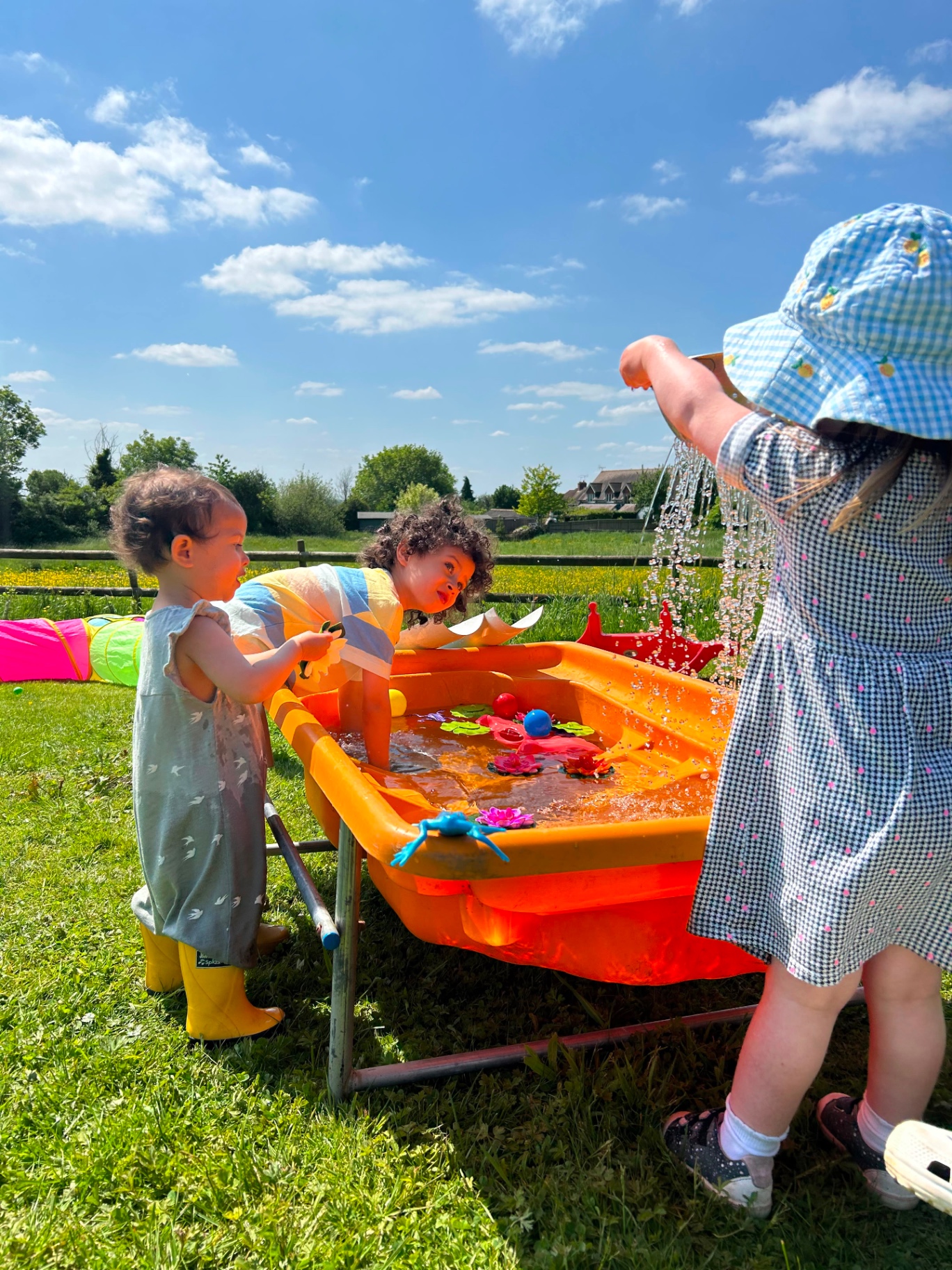 Children pouring water at an orange water table in a meadow